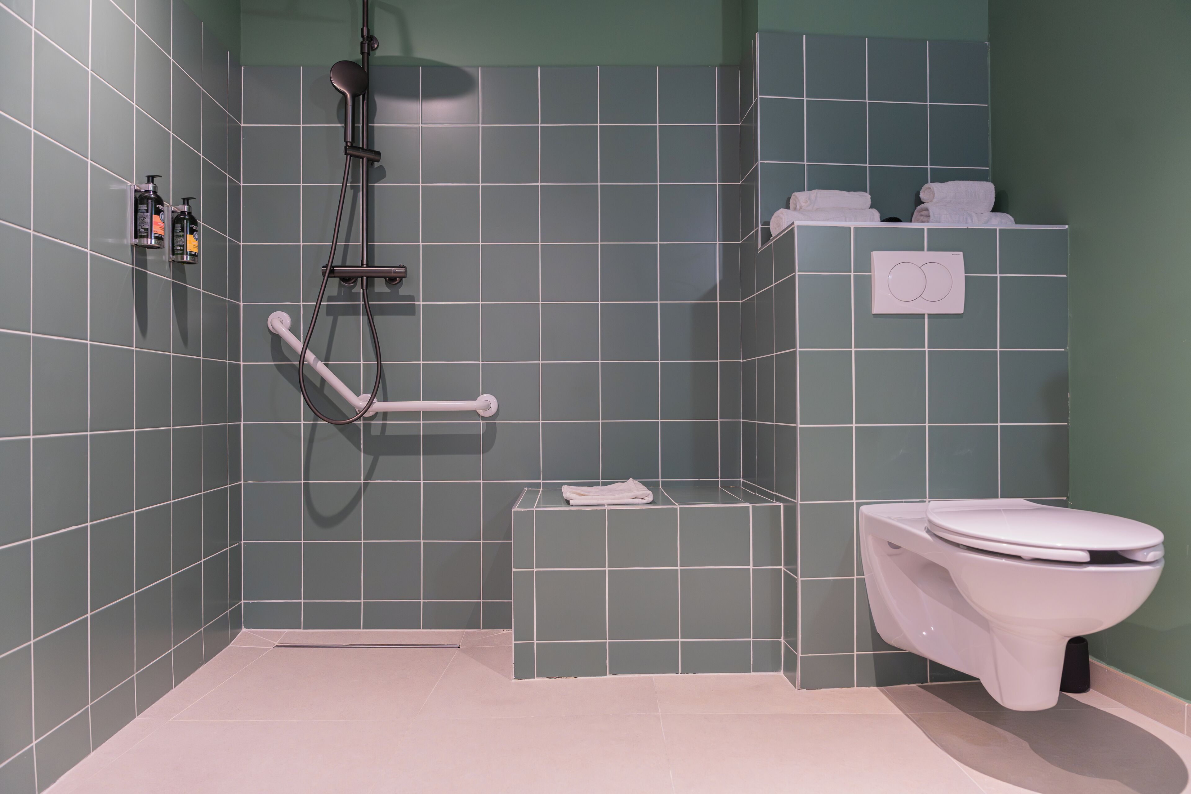 A bathroom with a shower, toilet, and a small shelf with towels.