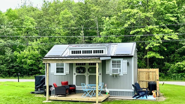 Une petite maison dotée de panneaux solaires, une véranda avec des meubles d’extérieur et une terrasse en bois.