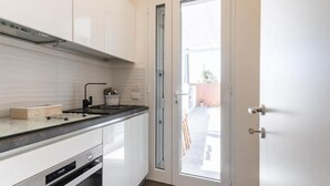 Cozinha com armários brancos, bancada preta e porta de vidro que dá para o exterior.