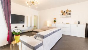 Uma sala moderna com um sofá, uma televisão, uma área de jantar e uma cozinha.