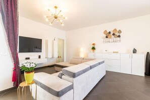 A modern living room with a sofa, a TV, a dining area, and a kitchen.