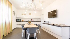 Cozinha moderna com armários brancos, uma mesa de jantar com cadeiras, uma televisão na parede e um candelabro.