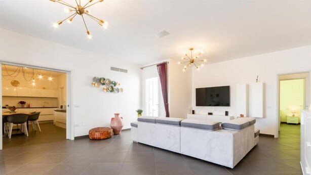 Uma sala de estar moderna com sofá, televisão e área de jantar com cadeiras e mesa.