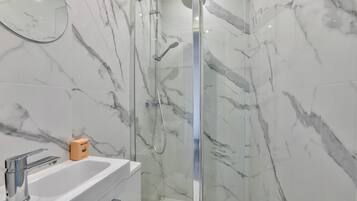 A modern bathroom with a glass-enclosed shower, a white sink, and marble walls.