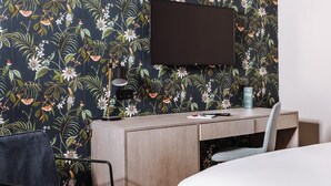 Camera d'albergo con una scrivania in legno, una sedia, un letto, una TV a schermo piatto montata a parete e carta da parati con motivi floreali.