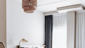 Una camera d'albergo moderna con un letto, una scrivania con una lampada, una finestra con tende e un pavimento in legno.