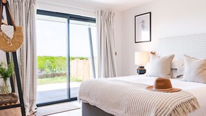 A bedroom with a bed, pillows, a hat, a lamp, and a framed picture on the wall. - The Lighthouse is an end of terrace four bedroomed seafront retreat with a hot tub and incredible vi (Widemouth Bay)
