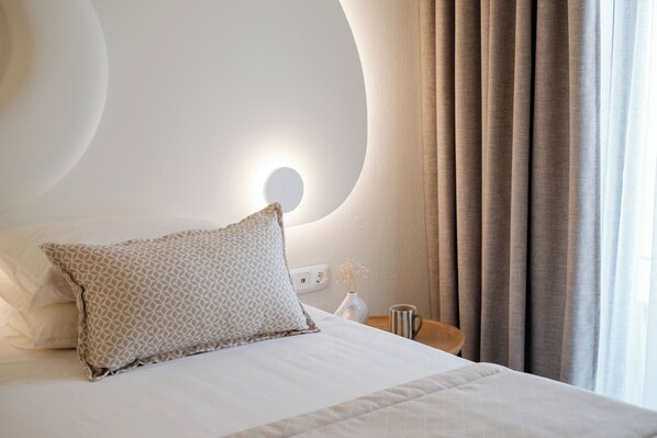 A neatly made bed with a patterned pillow, a bedside table with a vase, and a wall-mounted light fixture.