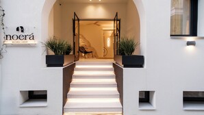 Una escalera conduce a un acceso con un letrero que dice 'noera NATURAL LUXURY'.