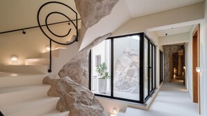 Una escalera moderna con un diseño singular que recuerda a las rocas, un cerramiento de cristal con una planta y un interior minimalista.