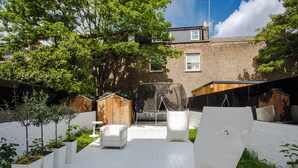 A modern outdoor patio with white furniture, a swing, and a white chair. - HUGE 5 floors townhouse in central London NW6 (London)
