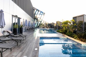 Un espace piscine extérieur moderne, doté de chaises longues et d’un espace salon fermé par des parois de verre.