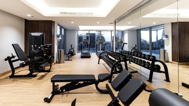 A modern gym with various exercise equipment, large windows, and a bright interior. - LUX 1BR Near B.khalifa (Dubai)