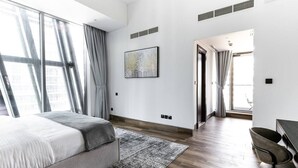 A modern hotel room with a large bed, a desk, and a view of the city through large windows. - Premium Corner Apt 1BD in Jone w Canal View (Dubai)
