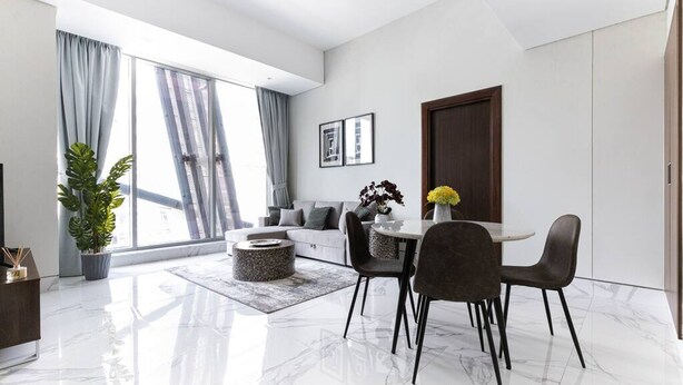 A modern living room with a dining area, large windows, and a view of the city. - Premium Corner Apt 1BD in Jone w Canal View (Dubai)