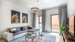 A modern living room with a sectional sofa, a glass coffee table, and artwork on the wall. - Pool View 1BR on Palm Jumeirah (Dubai)