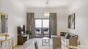 A modern living room with a sofa, TV, and dining area. - Pool View 1BR on Palm Jumeirah (Dubai)