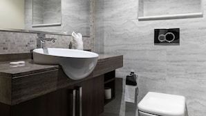 A modern bathroom with a large sink, dark wood vanity, marble walls, a toilet, and a towel rack. - LUX Waterfront 1BR Near B.khalifa (Dubai)