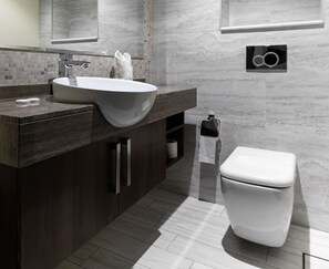 Une salle de bain moderne avec un grand lavabo, un meuble-lavabo en bois foncé, des murs en marbre, des toilettes et un porte-serviettes.