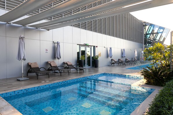 A modern indoor pool area with lounge chairs and a glass wall. - Stunning Corner Suite Canal View (Dubai)