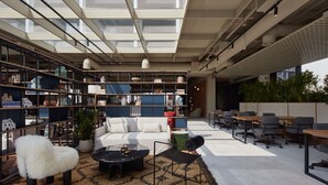 Een moderne kantoorruimte met een hoge plafond, dakramen, een witte bank, een bijzettafeltje en een boekenplank vol diverse voorwerpen.