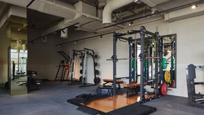 Een fitnessruimte met diverse gewichthefapparaten, waaronder een squatsrek en banken.