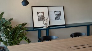 Een moderne kantoorruimte met een houten bureau, twee zwarte stoelen, een blauwe bank, een zwarte hanglamp en ingelijste foto's aan de muur.