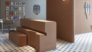 A modern reception area with a unique design, including a large brown desk, a wall-mounted display of artwork, and a patterned floor. - Deluxe Studio With Balcony Full Burj Khalifa View (Dubai)