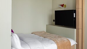 A neatly made bed with white and beige bedding, a television mounted on a wooden cabinet, and a red lamp on the wall. - Deluxe Studio With Balcony Full Burj Khalifa View (Dubai)