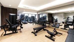 Ein modernes Fitnessstudio mit diversen Trainingsgeräten, großen Fenstern und Holzboden.