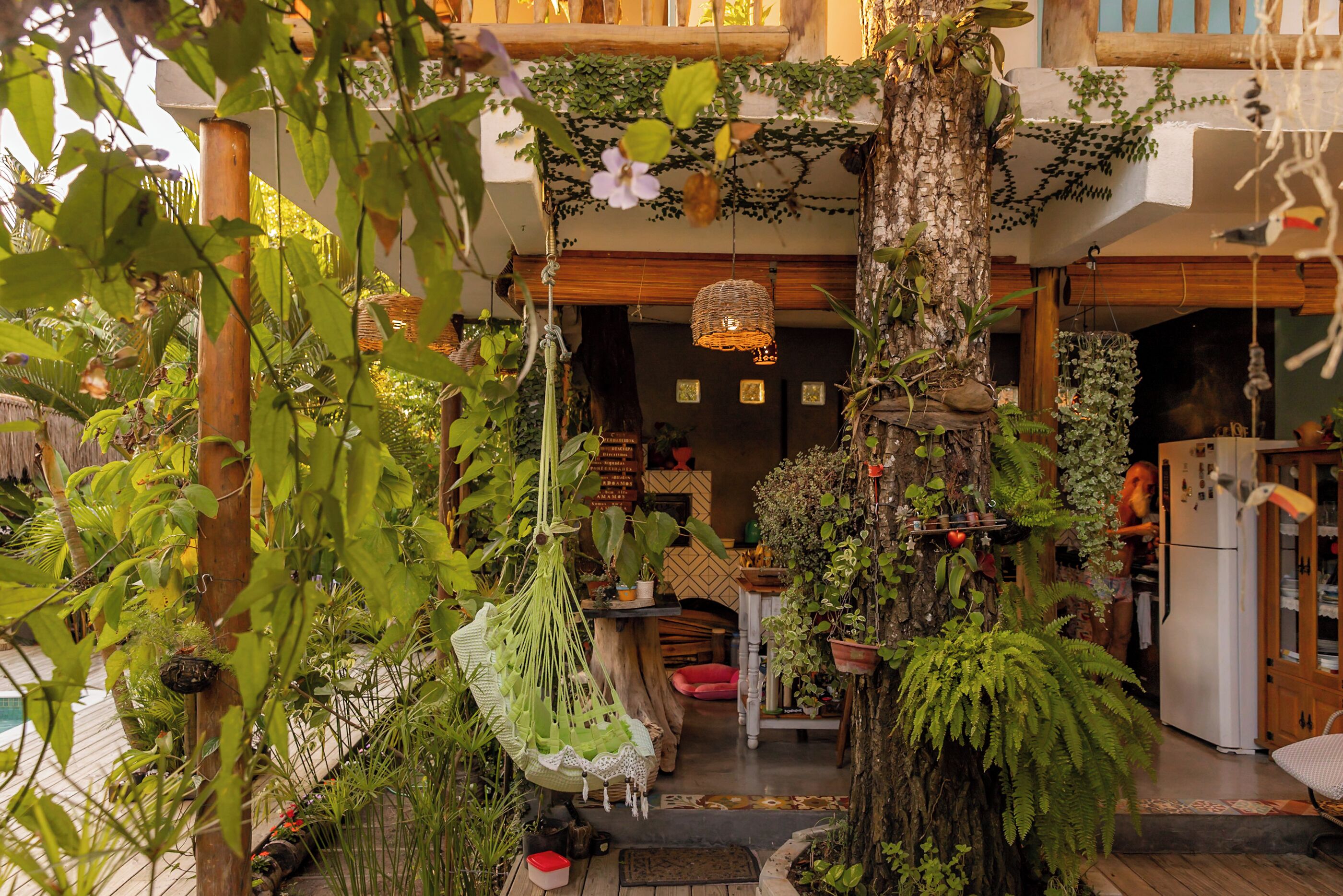 Un jardin intérieur luxuriant, agrémenté de fauteuils suspendus, d’une table en bois et d’un réfrigérateur.