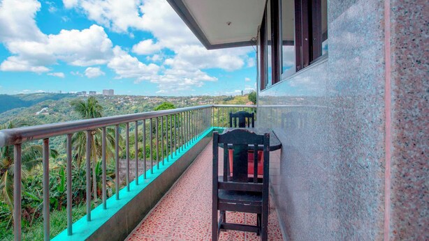 A balcony with a chair and a table, overlooking a mountainous landscape with greenery and a clear sky. - OYO 1140 Maganda Hotel (Tagaytay)