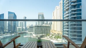 Een balkon met houten meubels en een bloempot, met uitzicht op een stadsgezicht met wolkenkrabbers en een jachthaven.