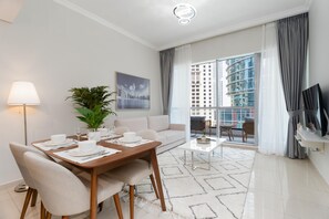 A modern living room with a dining area, a sofa, a coffee table, and a large window with a city view. - Fabulous 1 BR at Dubai Marina (Dubai)