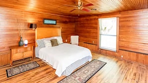 A wooden-paneled bedroom with a bed, nightstands, a ceiling fan, a window, and a wall-mounted TV.