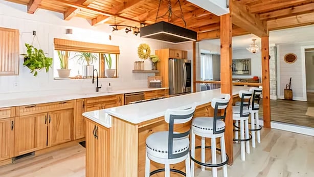A spacious kitchen with wooden cabinets, a large island with bar stools, and a stainless steel refrigerator.