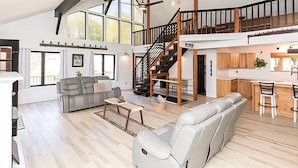 A spacious living area with a high ceiling, a staircase leading to an upper level, and a kitchen area with bar stools.