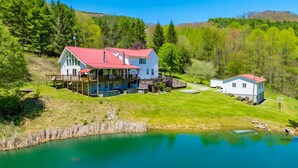A large house with a red roof, a deck, and a pond in front.
