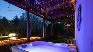 A hot tub with a wooden pergola overhead, surrounded by a wooden deck and a view of trees.