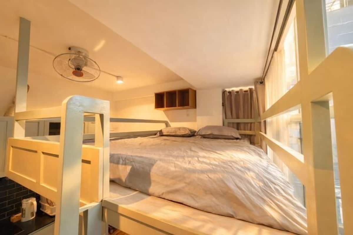 A dorm-style room with bunk beds, a desk, and a window.