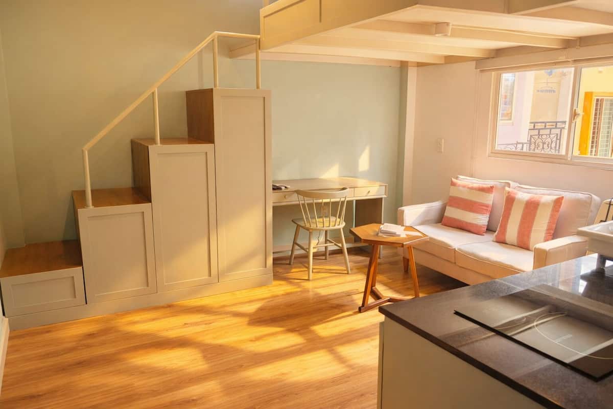A compact living space with a staircase, a dining area, a sofa, and a kitchen counter.