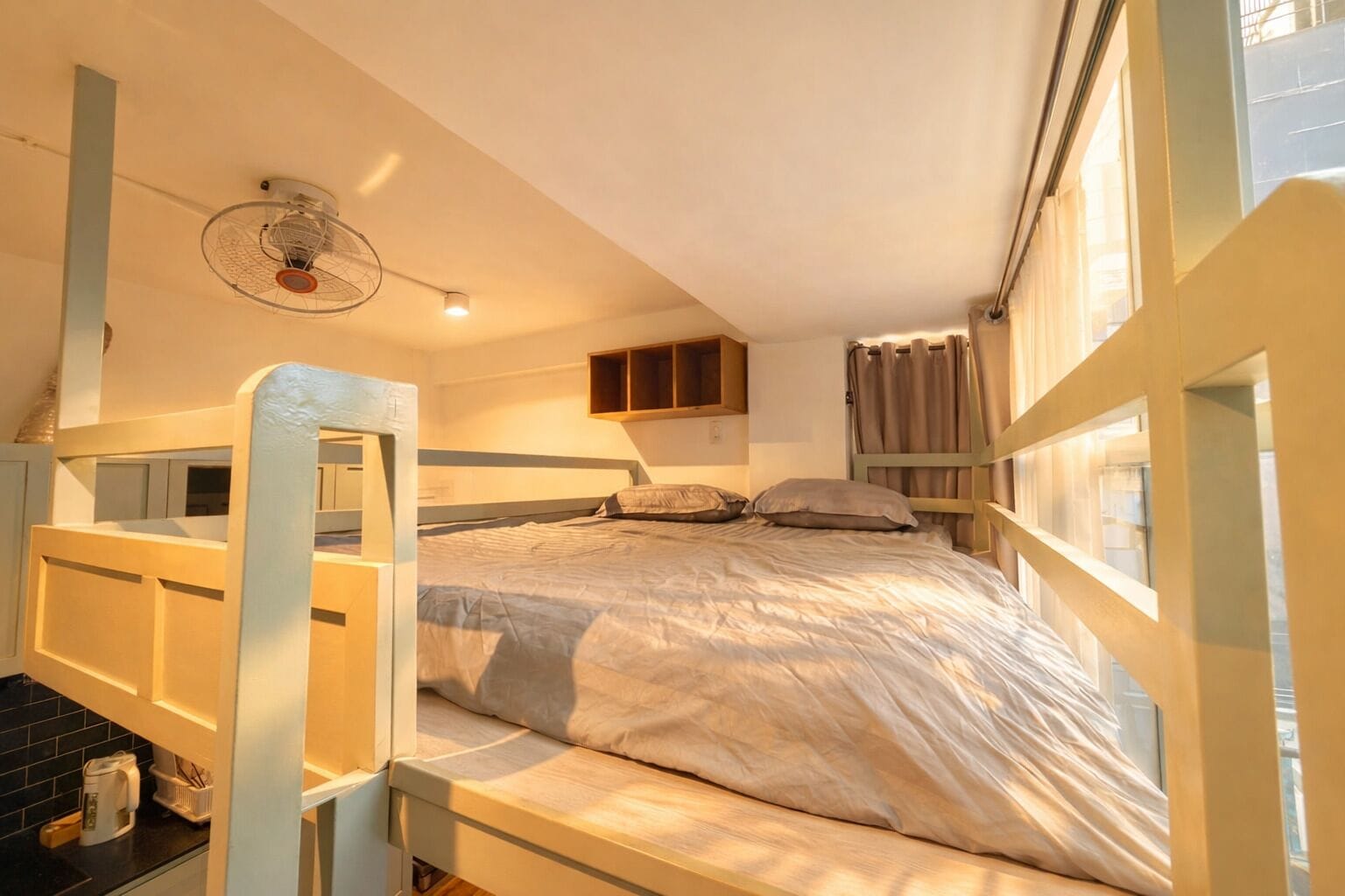 Habitación con literas, ventilador de techo, una estantería pequeña y ventana con cortinas.