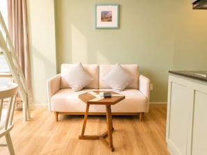 A room with a light green wall, a beige sofa with two pillows, a small wooden table with a remote control, and a framed picture above the sofa. - Signy House Hotel & Apartments Bach Dang River - Doan Nhu Hai (Ho Chi Minh City)