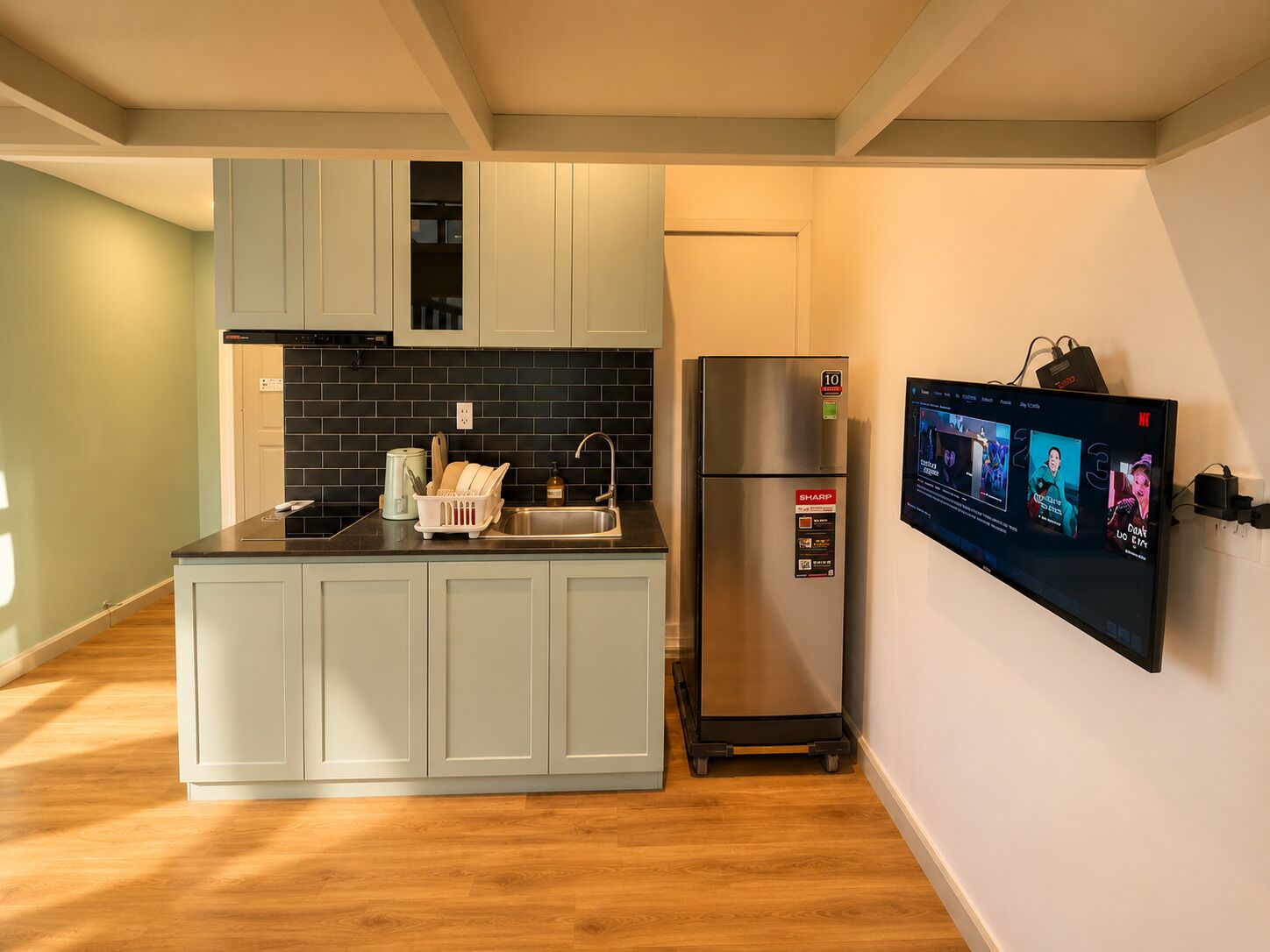 Una cocina moderna con armarios de colores claros, un refrigerador de acero inoxidable, un lavavajillas empotrado y un televisor de pantalla plana montado en la pared.