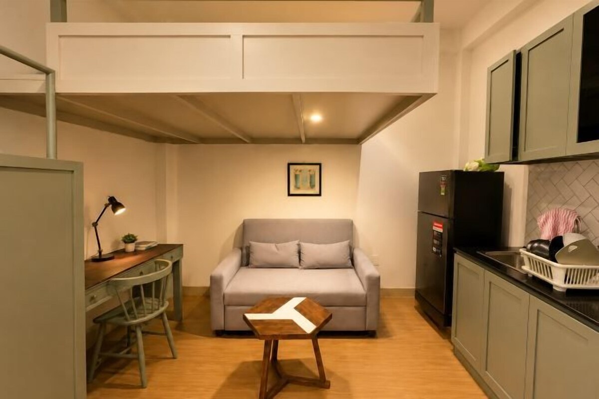 Un espacio habitable compacto con kitchenette, un sofá, una mesita y un escritorio con silla.
