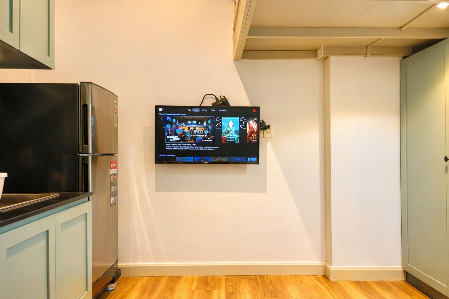 Eine Küche mit einem integrierten Kühlschrank, einem an der Wand befestigten Fernseher, der eine Speisekarte zeigt, und hellen Küchenschränken.