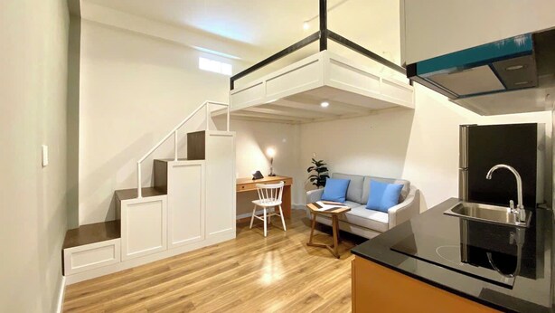 Un espacio habitable compacto con kitchenette, comedor y zona de estar con sofá y sillón.