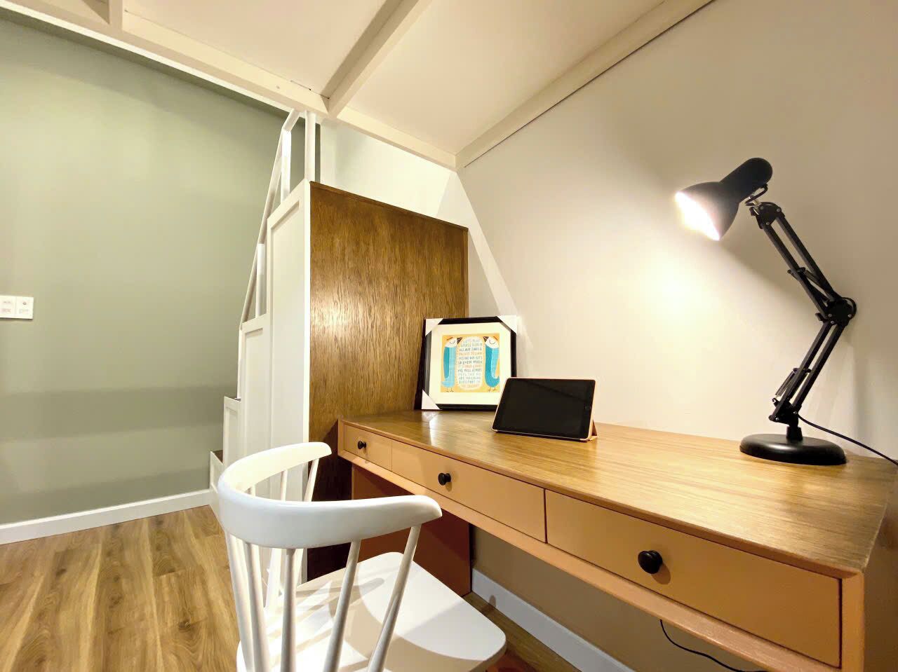 A small, well-lit room with a wooden desk, a white chair, a laptop, and a desk lamp.