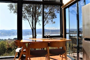 A dining area with a table and chairs, large windows with a view of a lake and mountains, and a modern interior design.