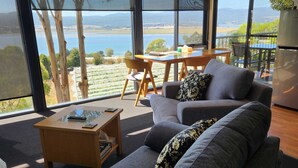 A modern living room with a large window, a sofa, a coffee table, and a dining area. - The Tamar Ridge Lookout at Tamar Ridge Apartments (Grindelwald)